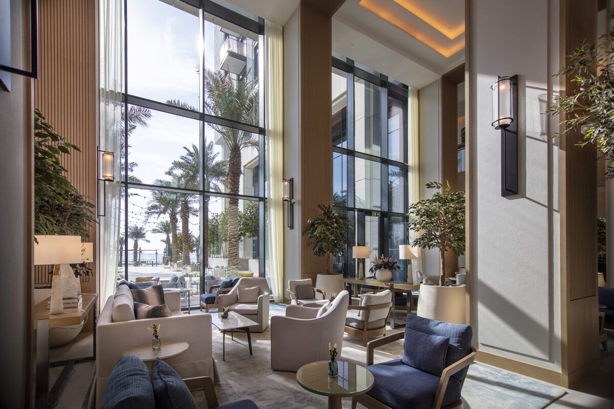 Luxuriöse Hotellobby mit großer Glasfassade und Blick auf den Garten mit Palmen.