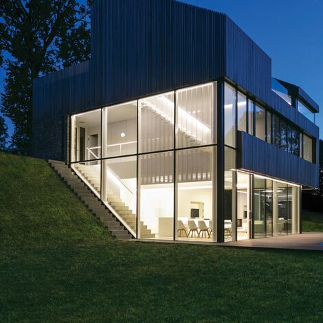 Maison privée bien éclairée avec beaucoup de verre la nuit.