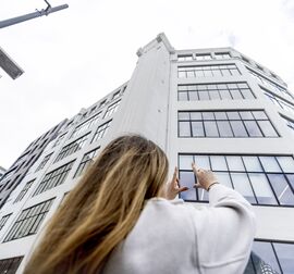 Blonde Frau vor einem weißen, mittelhohen Gebäude in der Stadt