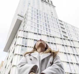 Frau blickt vor Hochhaus nach oben